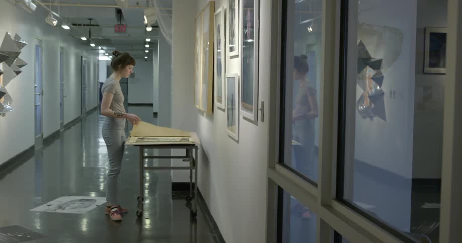 A woman standing in a hallway flips through large papers on a table