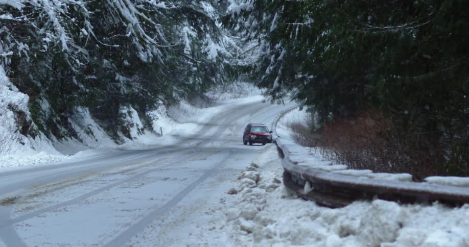 A crashed vehicle on the side of a snowy road flanked with evergreen trees