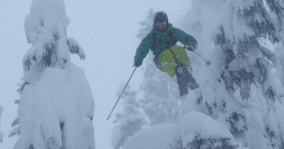 A skier does a huge jump through the forest in the falling snow