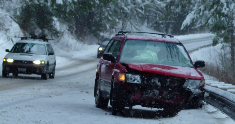 Traffic travels past a wrecked vehicle on a snowy road in the mountains