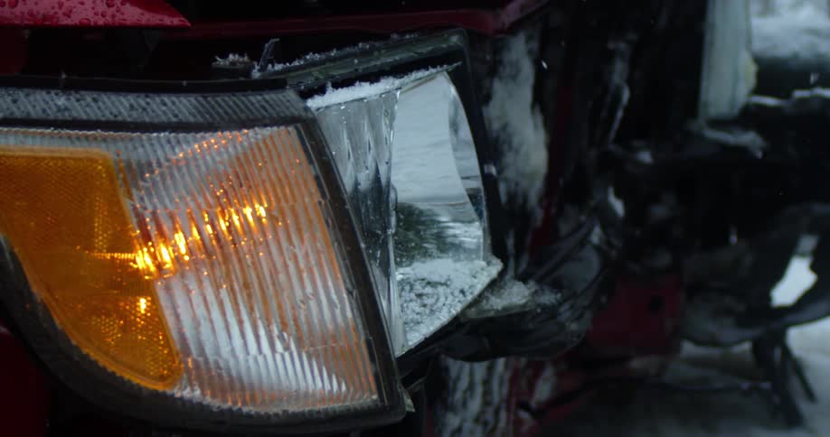 Snow falls onto the yellow blinking headlight of a parked car