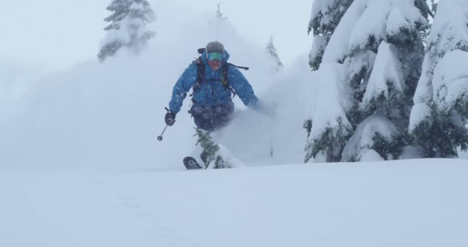 A skier sends up a cloud of snow as they ski through heavy falling snow