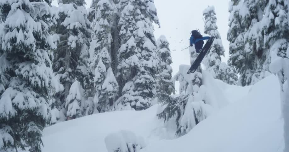 A skier does a huge jump over a snowy tree