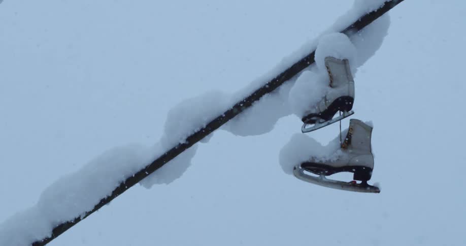 Snow falling around ice skates hanging from a power line