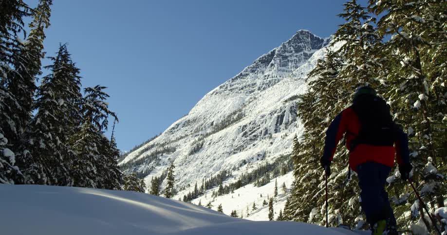 A skier moves towards huge mountains in the sun