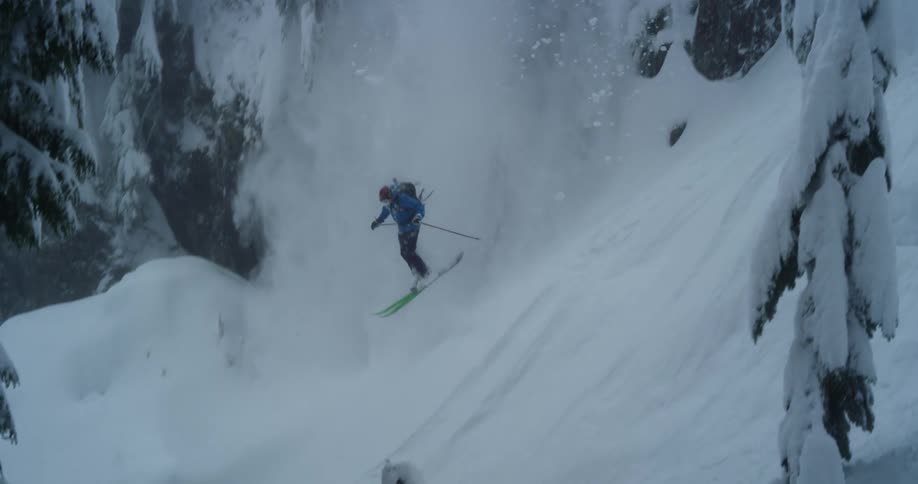 Skier jumps down from the snow covered cliff in the mountains causing a small avalanche