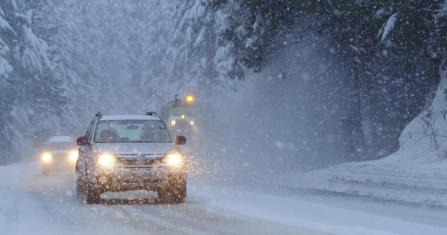 Two cars drive by a snow plow in heavy snow