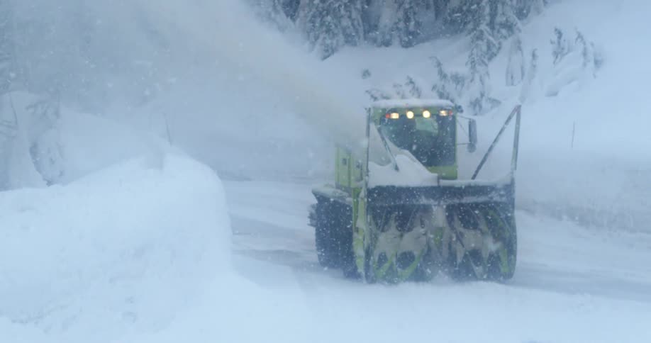 A snow plow cleaning a street while it snows heavily