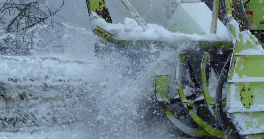 A snow blower removing snow outside near trees