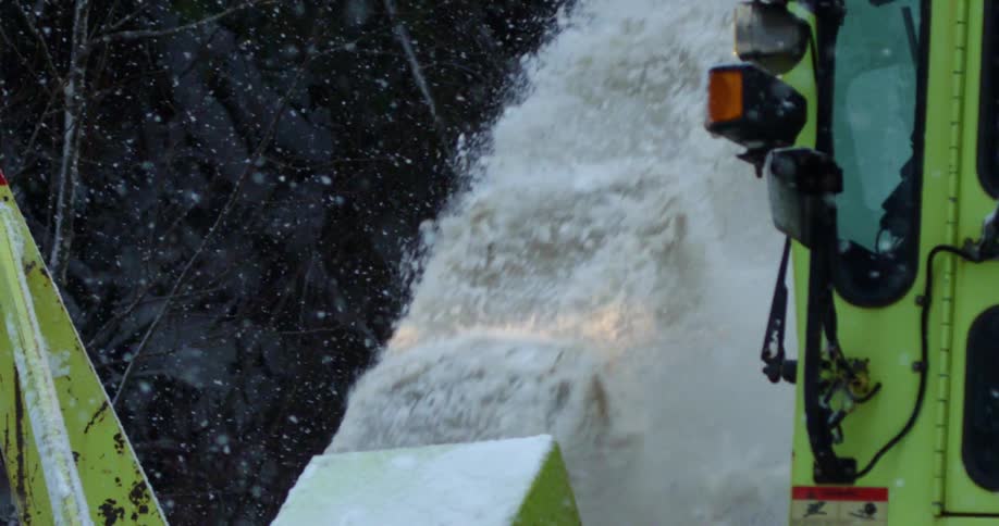 Snow blowing out of a snow plow as it drives along