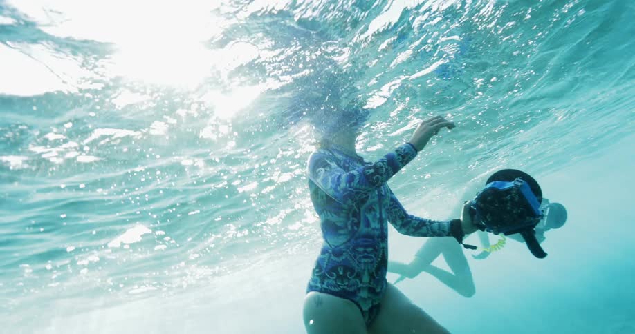 A man and woman hold large underwater cameras while swimming in the ocean