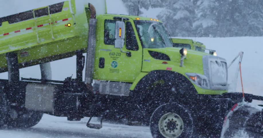 Snow plows driving down a snowy street as snow falls