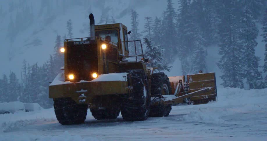 A snow plow operating on a snowy night