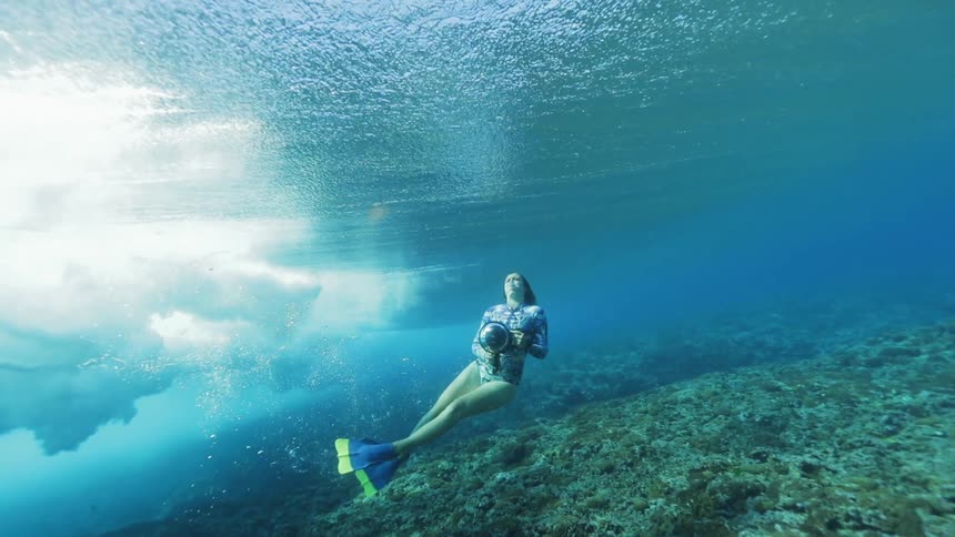 A woman films waves from under clear blue water