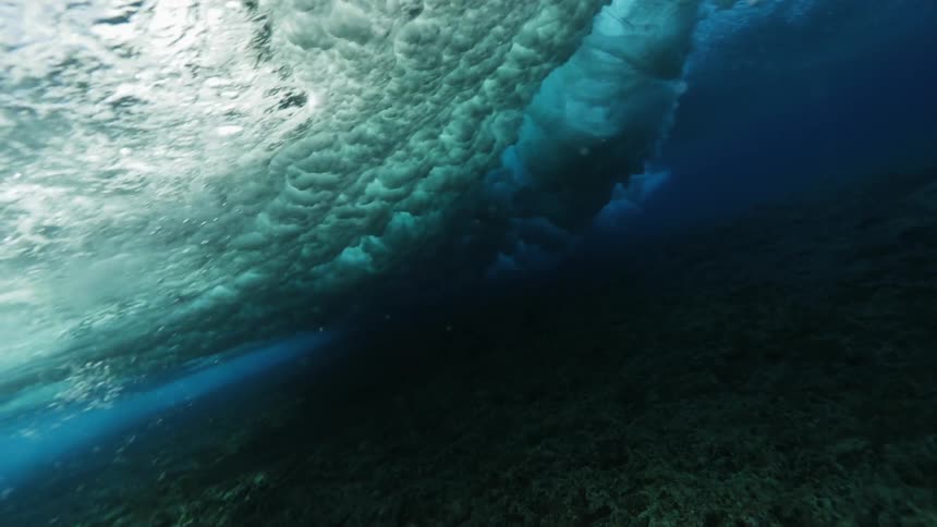 A heavy wave rolls over a swimmer in a shallow reef