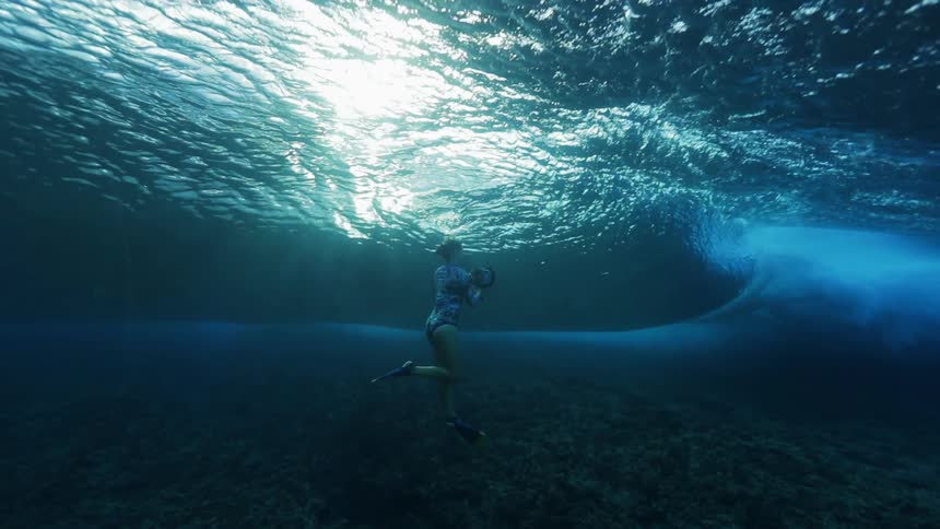 A woman films a wave rolling over her head underwater