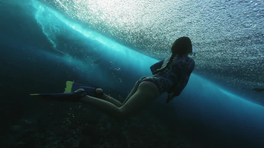 Two people are swimming underwater filming surfers