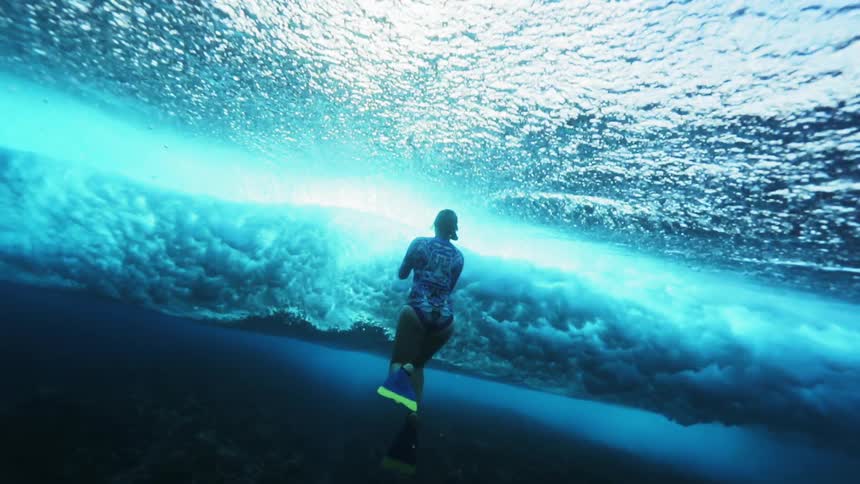 Female diver films underwater waves passing over her in the blue ocean waters