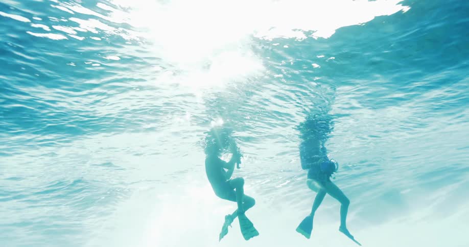 Two people are swimming underwater in the glinting sun
