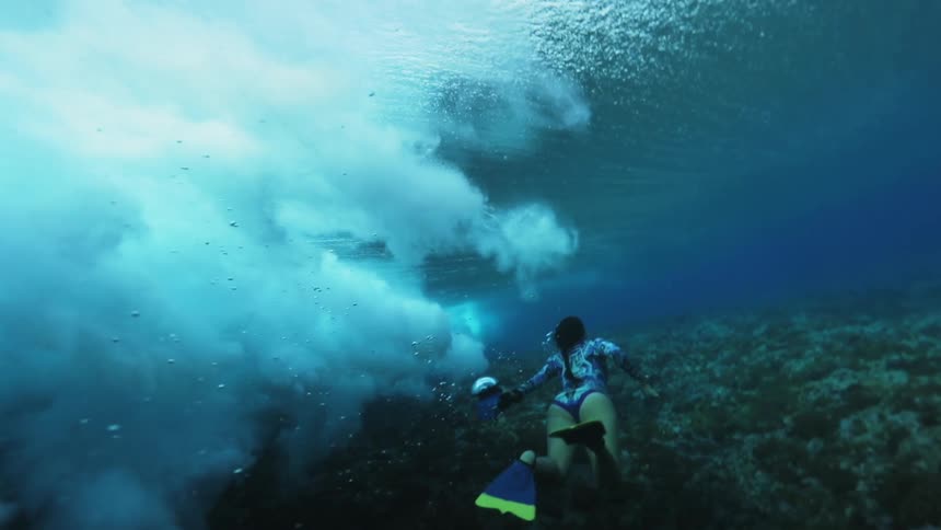 Waves crashing around a woman swimming underwater as camera spins