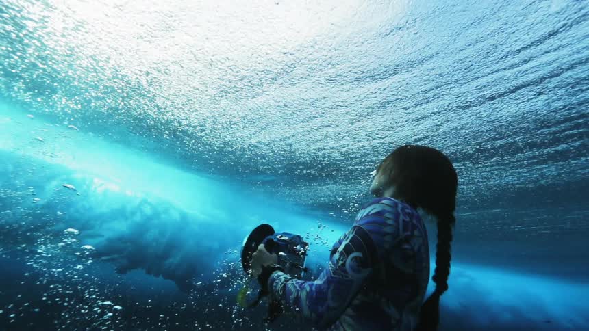 A woman swimming underwater as a wave rolls overhead