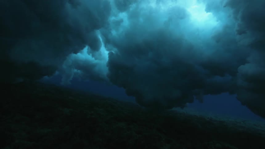 An ocean wave creates clouds of bubbles underwater as it passes overhead