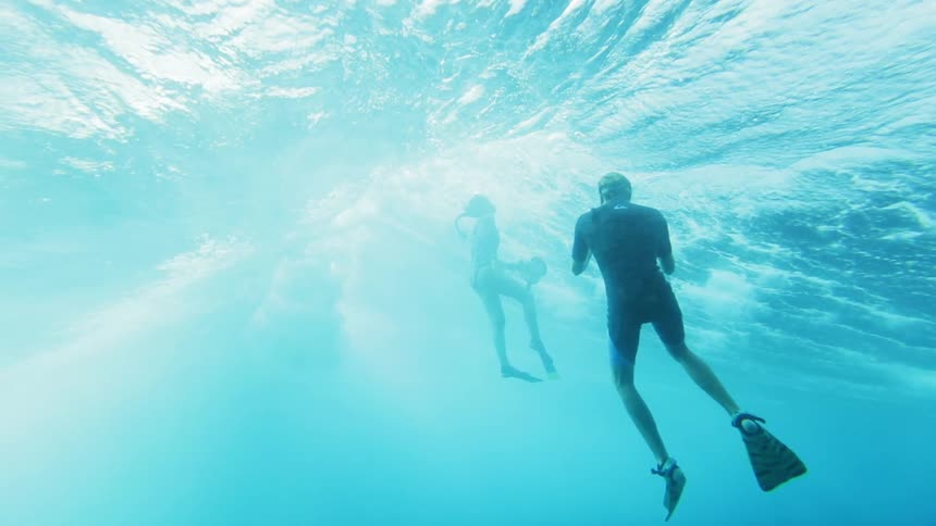 A man underwater takes pictures of a woman in the waves