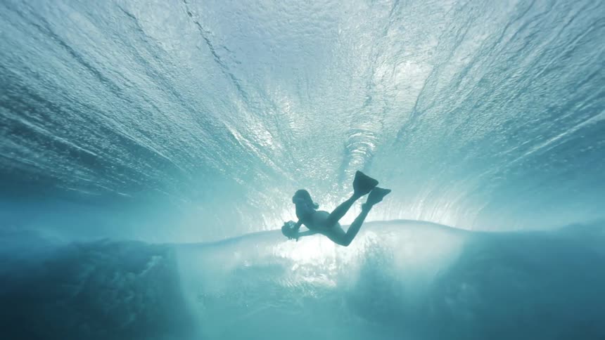 A swimmer with a camera is backlit as a wave rolls overhead