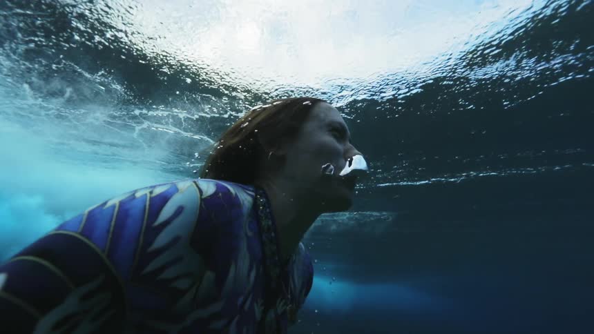 A woman swimming underwater with a camera then rising to the surface