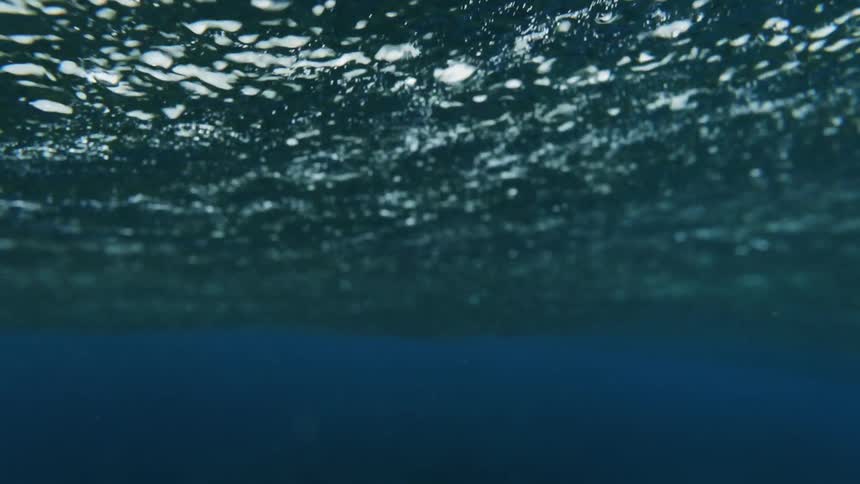 Blue bubbly ocean water waves gently roll above the the deep blue waters below