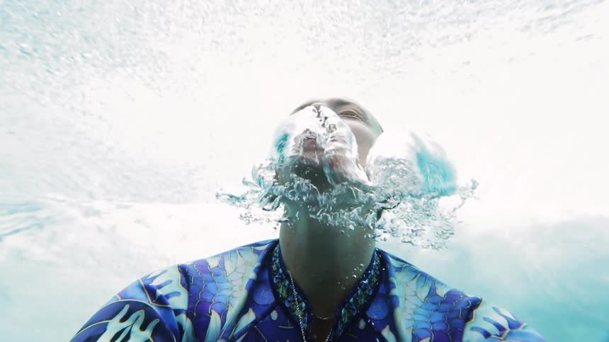 A woman blowing bubbles underwater and then putting her head above the surface