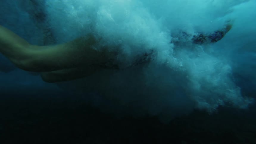 Woman swims underwater as wave passes overhead and catches her in its wake