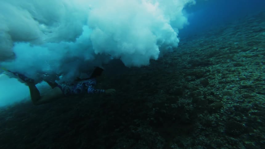 A woman underwater swims through crashing waves