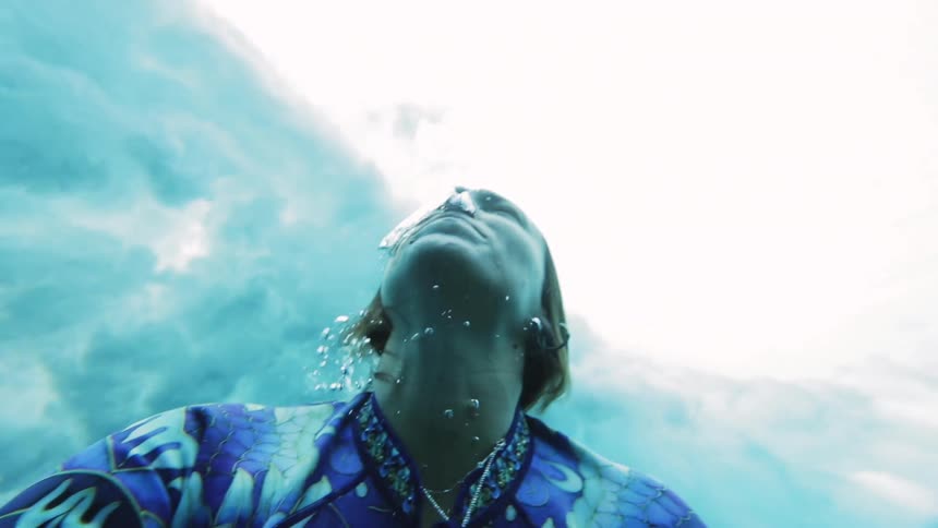 A person swims in water as heavy wave crashes above