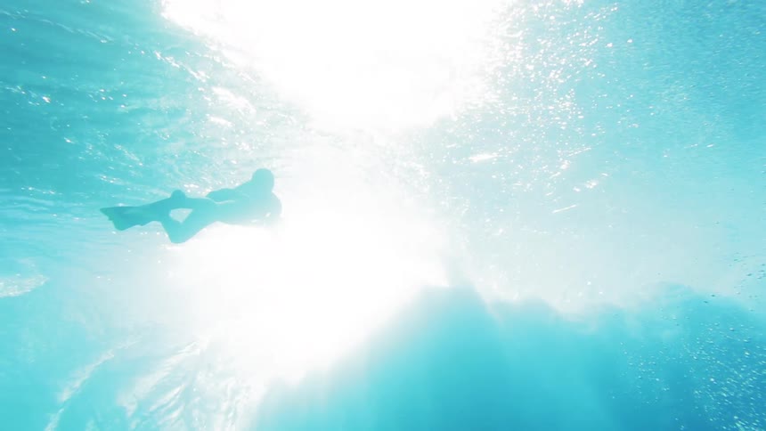 A woman swimming under water as a wave rolls by