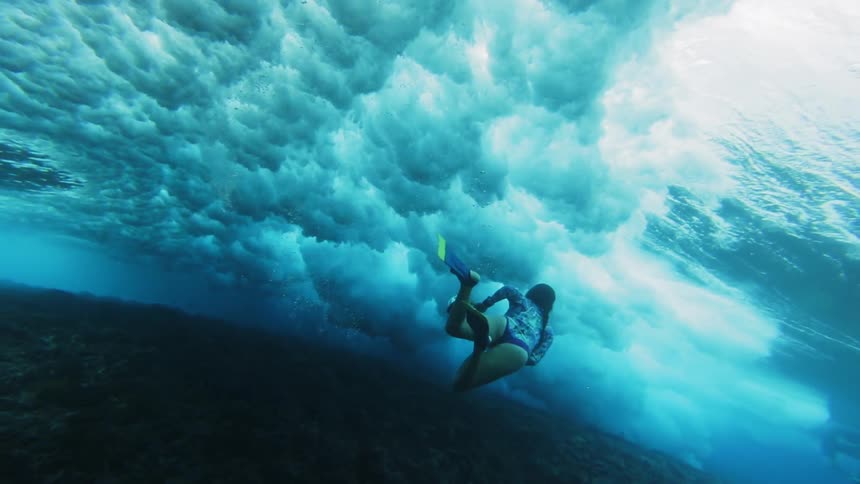 A woman swims towards a massive wave underwater