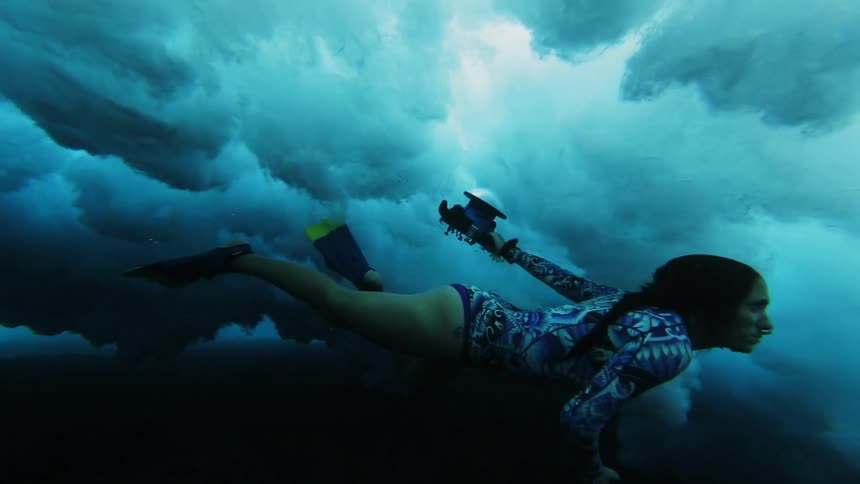 Woman swims underwater just over the seabed becoming enveloped in turbulence from wave crashing overhead