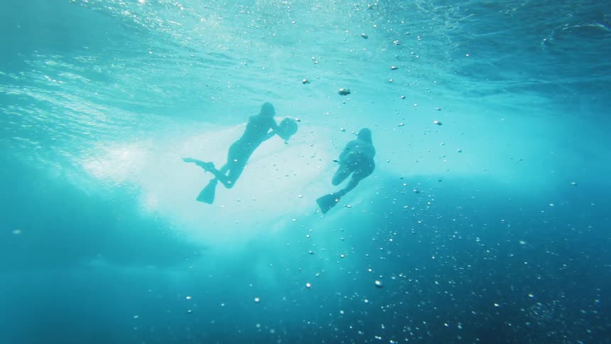Two underwater people photograph a surfer on the wave above them
