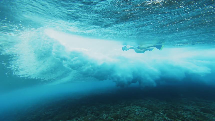 Two people are swimming underwater in the ocean filming waves