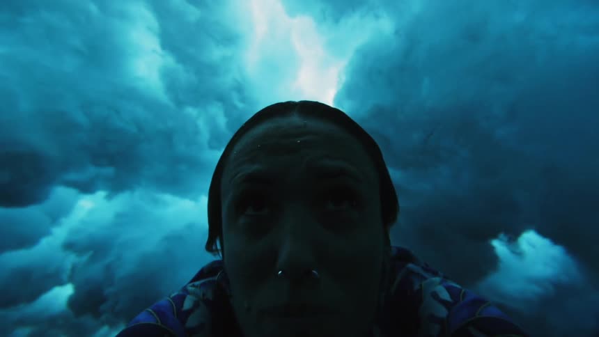 Woman swimming underwater is enveloped by foam created by crashing wave