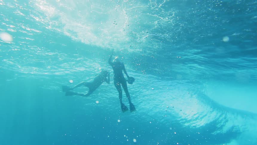 A man and woman swimming under water in the waves with cameras