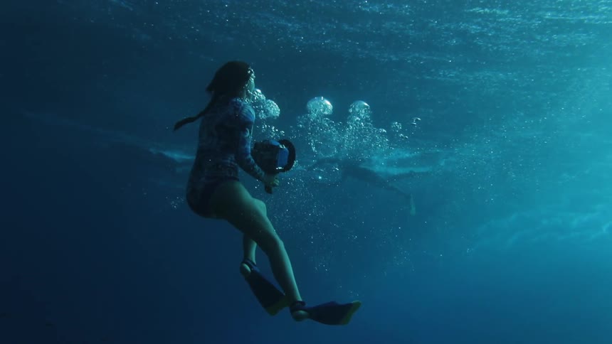 A woman swims underwater with a camera in deep blue water
