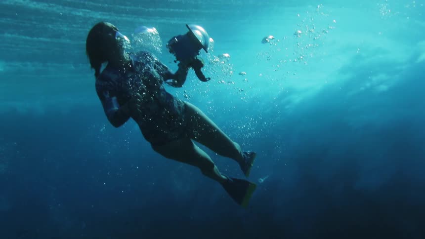 A female diver films an ocean wave from beneath the sea with an underwater camera before swimming up