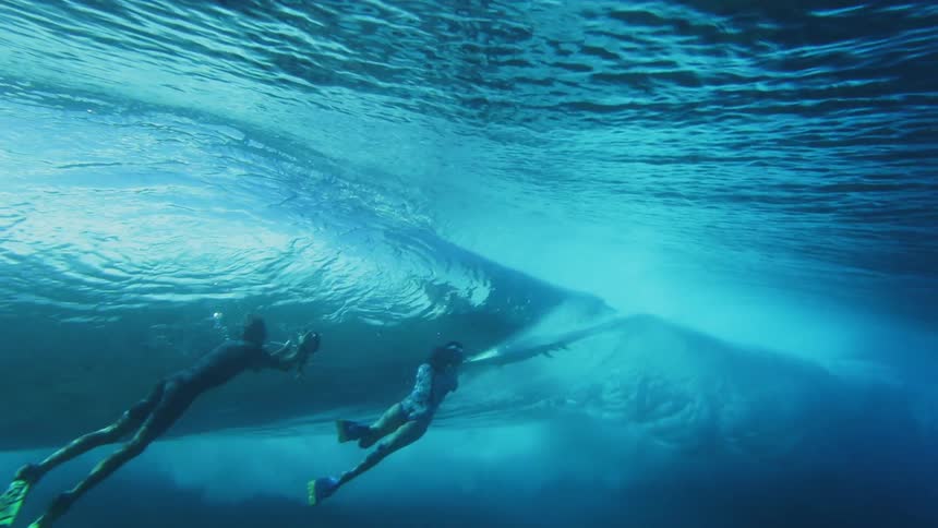 A man and woman swim underwater and take photographs of a surfer on a wave