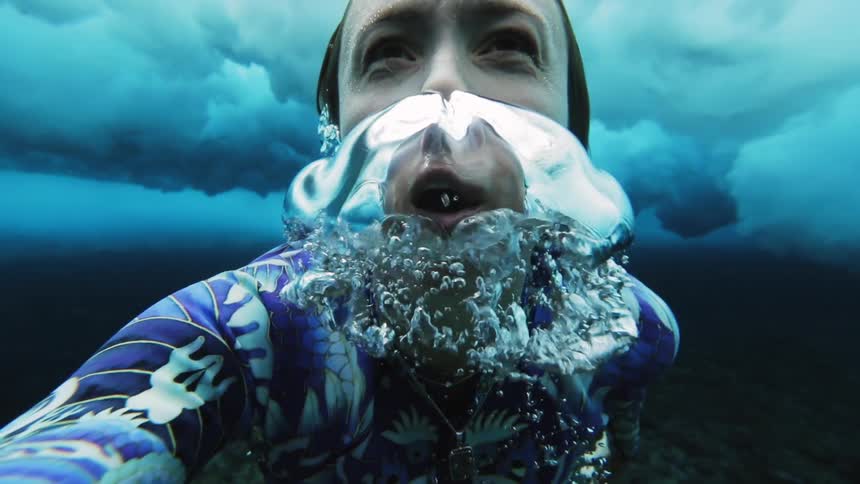 Young woman dives under a wave and breaks the surface of the blue ocean waters
