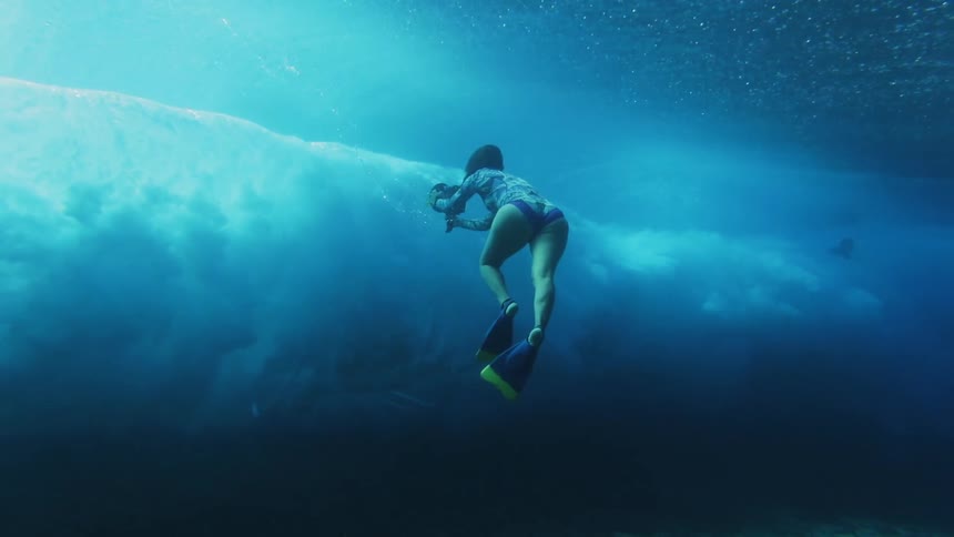 A woman underwater takes photos of a huge wave overhead