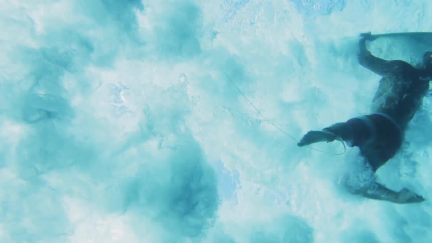 Underwater footage of a surfer falling off a surfboard in the clear ocean waters