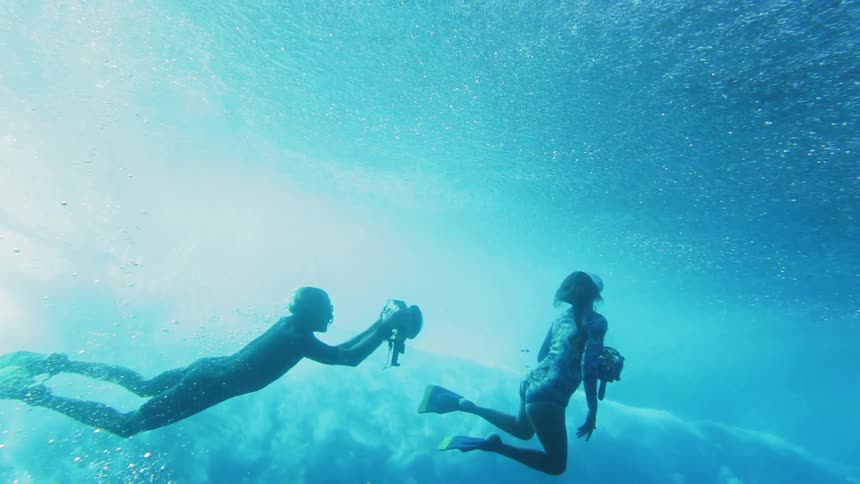 Underwater footage of swimmers filming the waves passing on the surface of the blue ocean waters