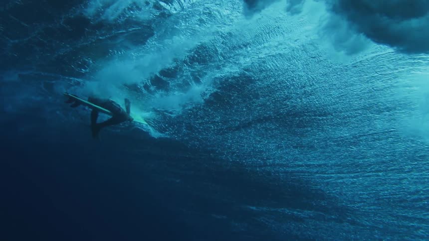 A strong wave moves past a man paddling a surfboard under the surface of the ocean