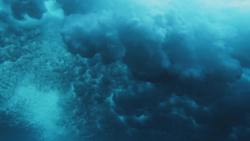 A woman swims through the dark clouds of an ocean wave